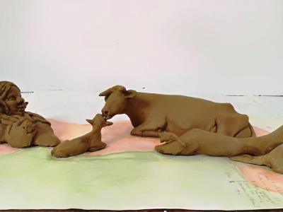 Kunstskulptur eines freundlichen Riesens, der auf dem Rücken liegt und eine Kuh, die liebevoll ihr Kalb abschleckt