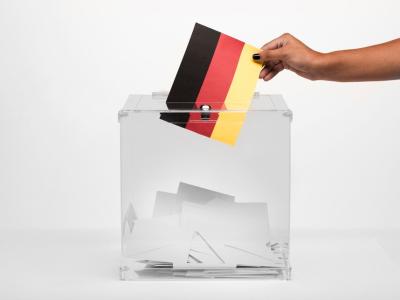 Ein Mensch wirft einen Zettel in Deutschlandfarben in eine Wahlurne